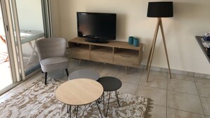 Een woonkamer met een televisie, een stoel, een klein tafeltje en een vloerlamp.