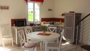 Une cuisine avec un coin repas, des meubles blancs, un crédence carrelée en rouge et blanc, un four à micro-ondes et une fenêtre donnant sur un espace verdoyant.