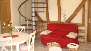 Un escalier en colimaçon, un canapé rouge, une table blanche ornée d’un vase de fleurs et un mur en briques.