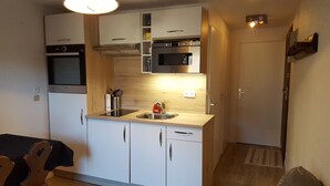 A compact kitchen with white cabinets, a built-in oven, a microwave, and a sink. - Beautiful T2 comfortable near the ski slopes (Saint-Gervais-les-Bains)