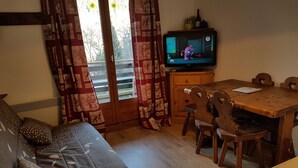 A living room with a sofa, wooden dining table, chairs, a television, and curtains. - Beautiful T2 comfortable near the ski slopes (Saint-Gervais-les-Bains)