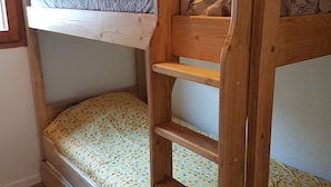 A wooden bunk bed with a patterned pillow and a plain pillow. - Beautiful T2 comfortable near the ski slopes (Saint-Gervais-les-Bains)