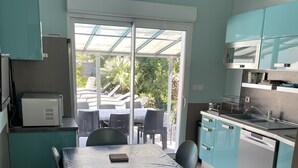 Una cocina moderna con armarios color turquesa, un comedor con mesa y sillas, y vistas al exterior a través de un ventanal.