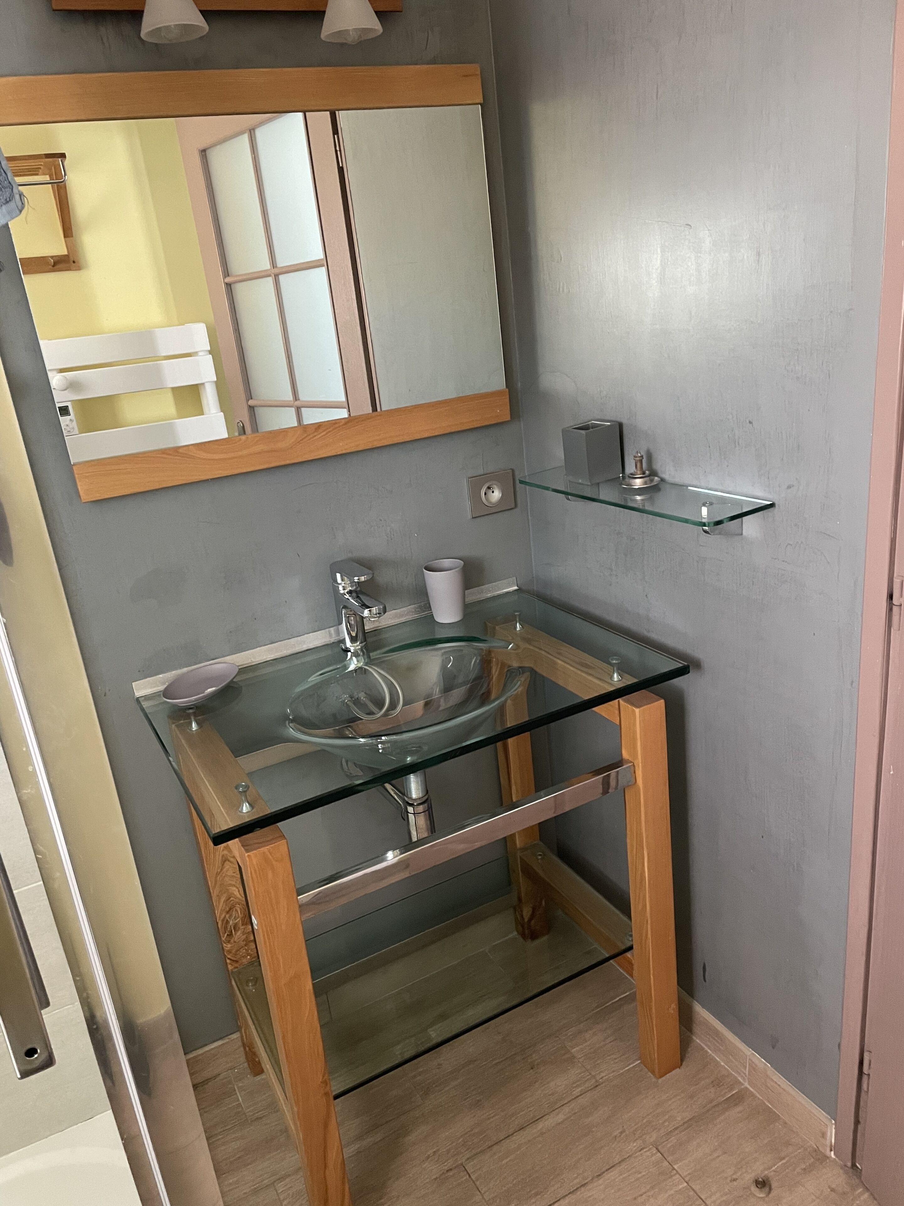 A bathroom with a glass sink, wooden base, and a mirror above.