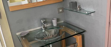A bathroom with a glass sink, wooden base, and a mirror above.
