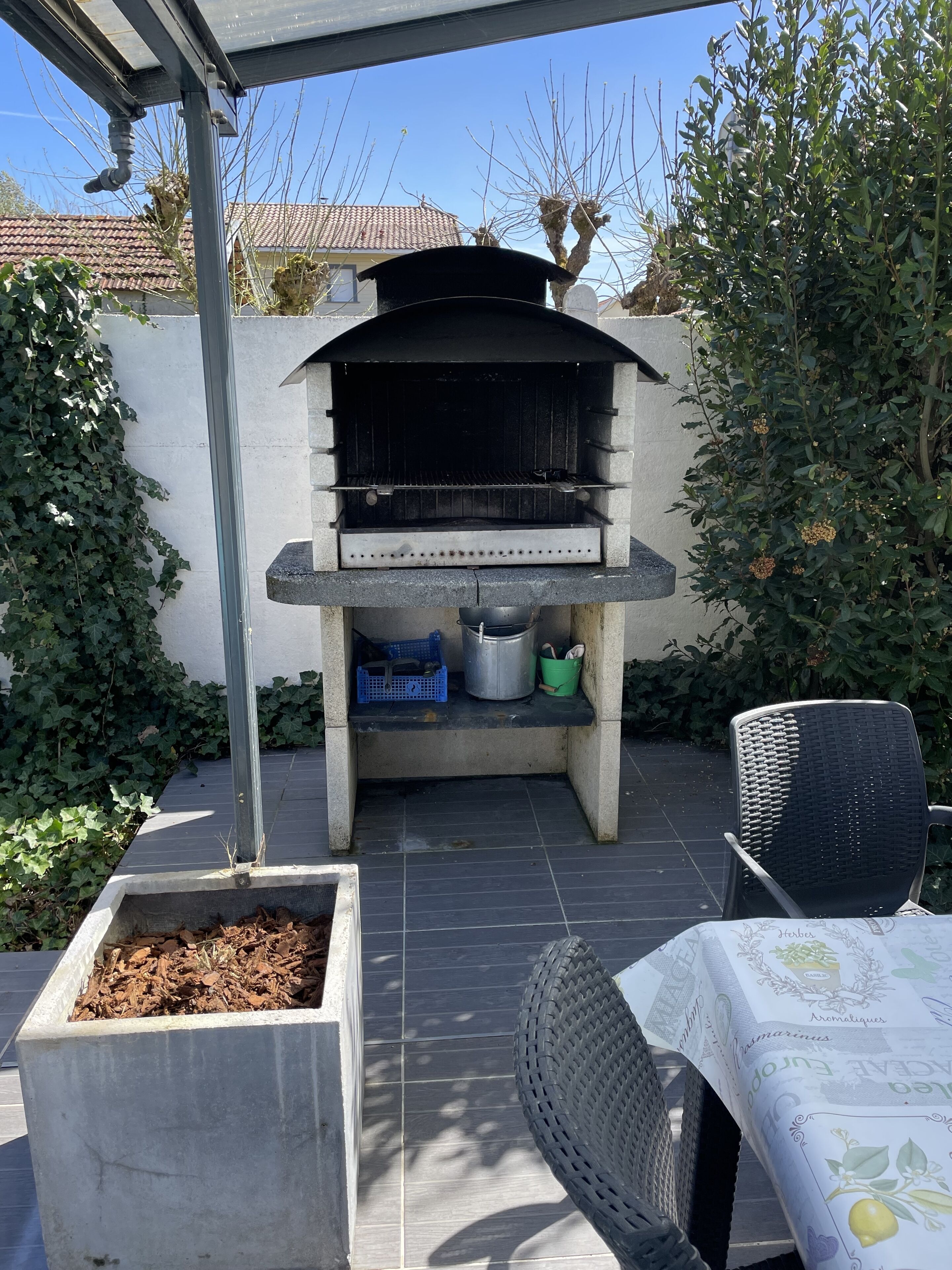 Un patio exterior con una parrilla empotrada, zona de estar y jardineras.
