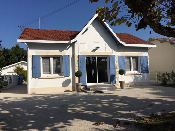 A two-story house with a red-tiled roof, blue shutters, and a small front porch.