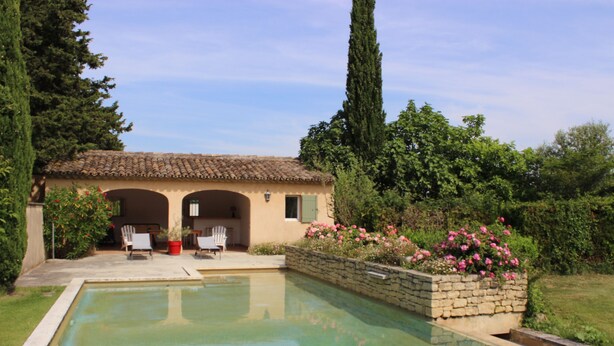 Una piscina con una parete in pietra e un patio con sedie e un tavolo.