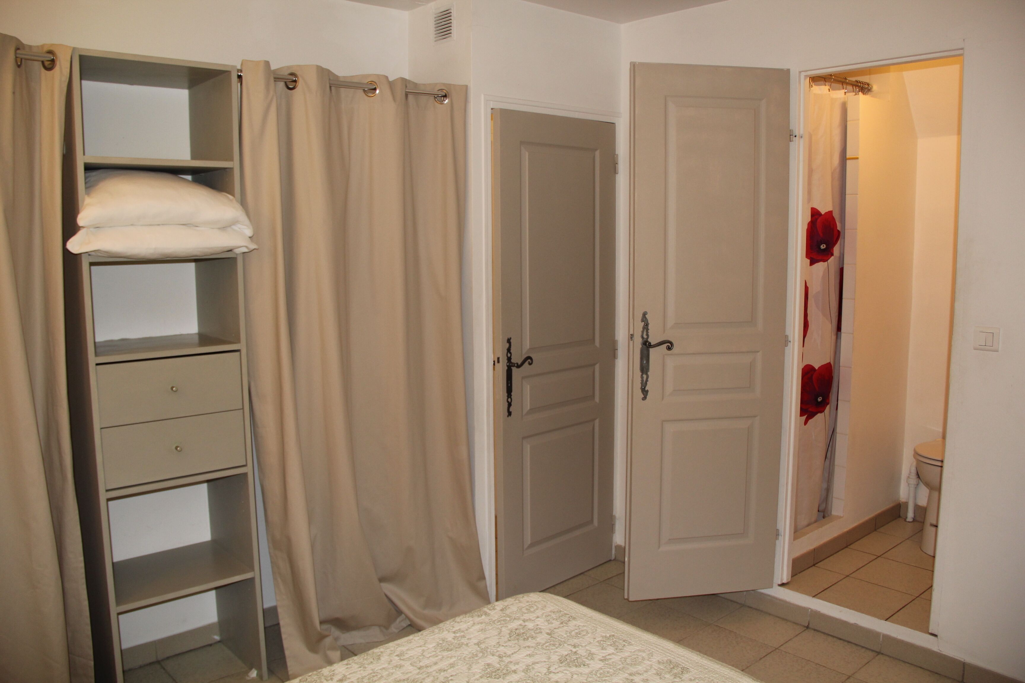 A bedroom with a bed, a wardrobe, and a bathroom with a shower curtain.