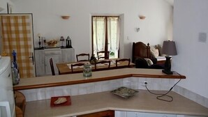 Una cucina compatta con zona pranzo, che include un'isola piccola, un tavolo con sedie e una finestra con tende.