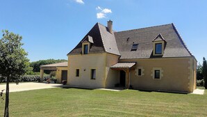 Ein zweistöckiges Haus mit geneigtem Dach, einer überdachten Veranda und einem gepflegten Rasen.