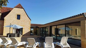 Ein Gebäude mit einer Steinfassade, einem Glasanbau und Außenplätzen mit Stühlen und Sonnenschirm.