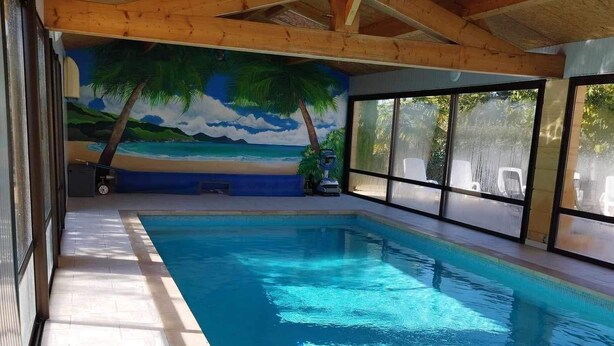 Ein hallenbad mit Holzbalkendecke, gefliestem Boden und einem Wandgemälde mit Strandmotiv.