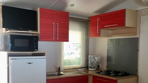 Eine kleine Küche mit Kühlschrank, Mikrowelle, Herd und roten Schränken.