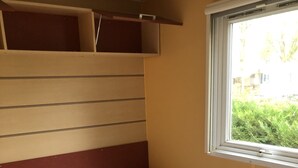 Ein Zimmer mit zwei Einzelbetten, jeweils mit Kissen und Decke ausgestattet. Ein kleiner Nachttisch und ein Fenster mit Blick ins Grüne sind ebenfalls vorhanden.