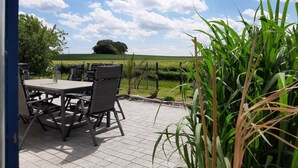 An outdoor patio with a table and chairs, surrounded by greenery and a view of a field. - family-friendly non-smoking house with large garden and beautiful view (Ralswiek OT Gnies)