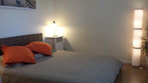 Un dormitorio con una cama, dos almohadas, una mesita de noche con lámpara y una lámpara de pared.