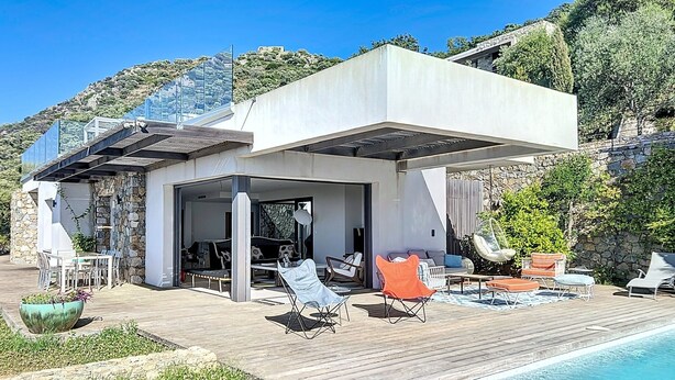 A modern villa with a pool, outdoor seating, and a stone wall backdrop. - Luxury villa, sea view - swimming pool facing the sunset (Corbara)