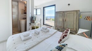 A bedroom with a bed, a desk, a wardrobe, and a view of the sea. - Luxury villa, sea view - swimming pool facing the sunset (Corbara)