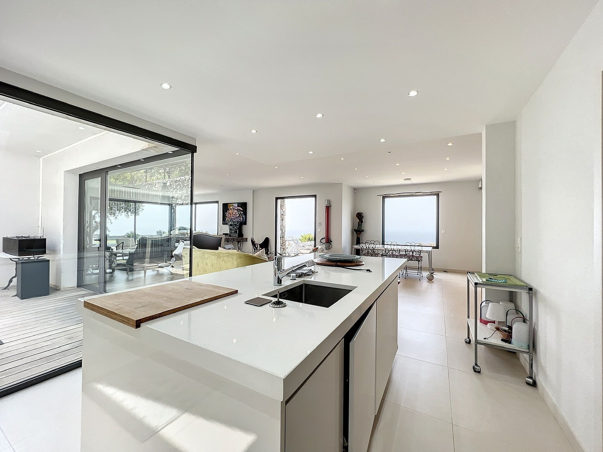 A modern kitchen with a large island, a dining area with a glass wall, and a view of the outdoors.
