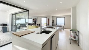 A modern kitchen with a large island, a dining area with a glass wall, and a view of the outdoors. - Luxury villa, sea view - swimming pool facing the sunset (Corbara)