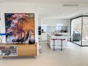 A modern kitchen with white cabinets, a large abstract painting, and a bar area with stools.