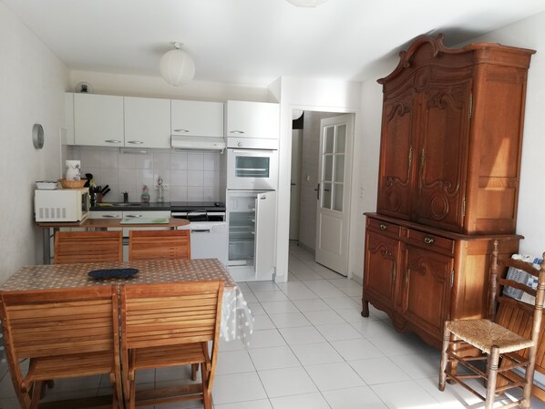 Una cocina compacta con armarios blancos, un microondas y una mesa de comedor de madera con sillas.