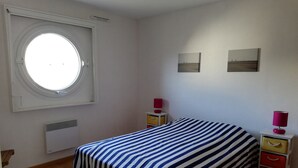 Une chambre à coucher comprenant un lit, une fenêtre, un radiateur et deux tables de chevet avec des lampes.