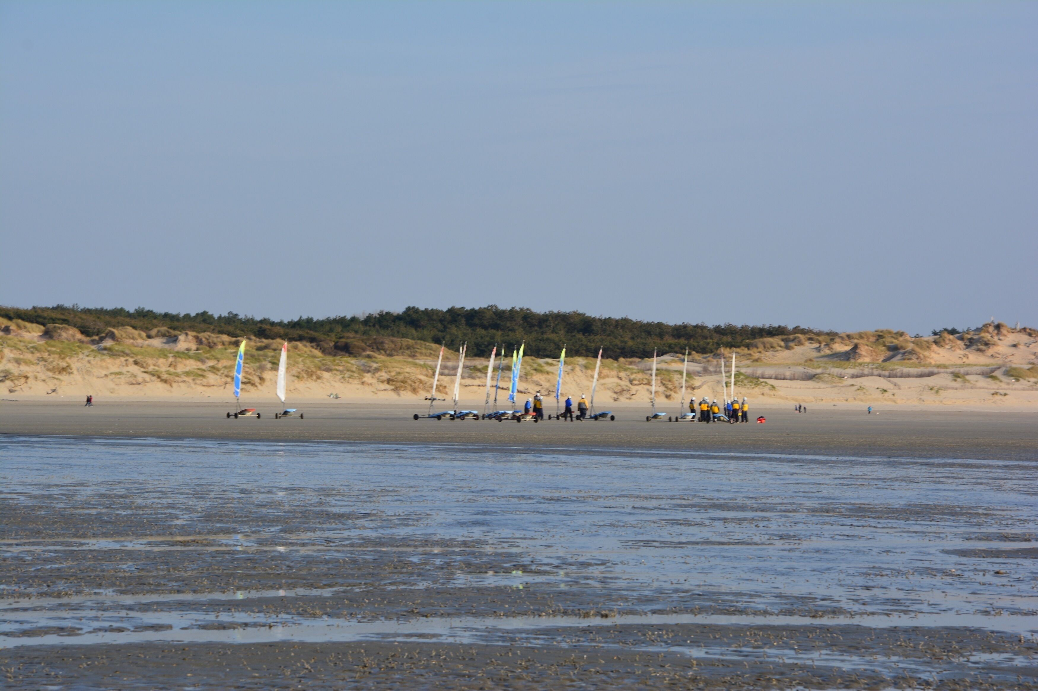 Een strand met verschillende zeilboten en mensen.