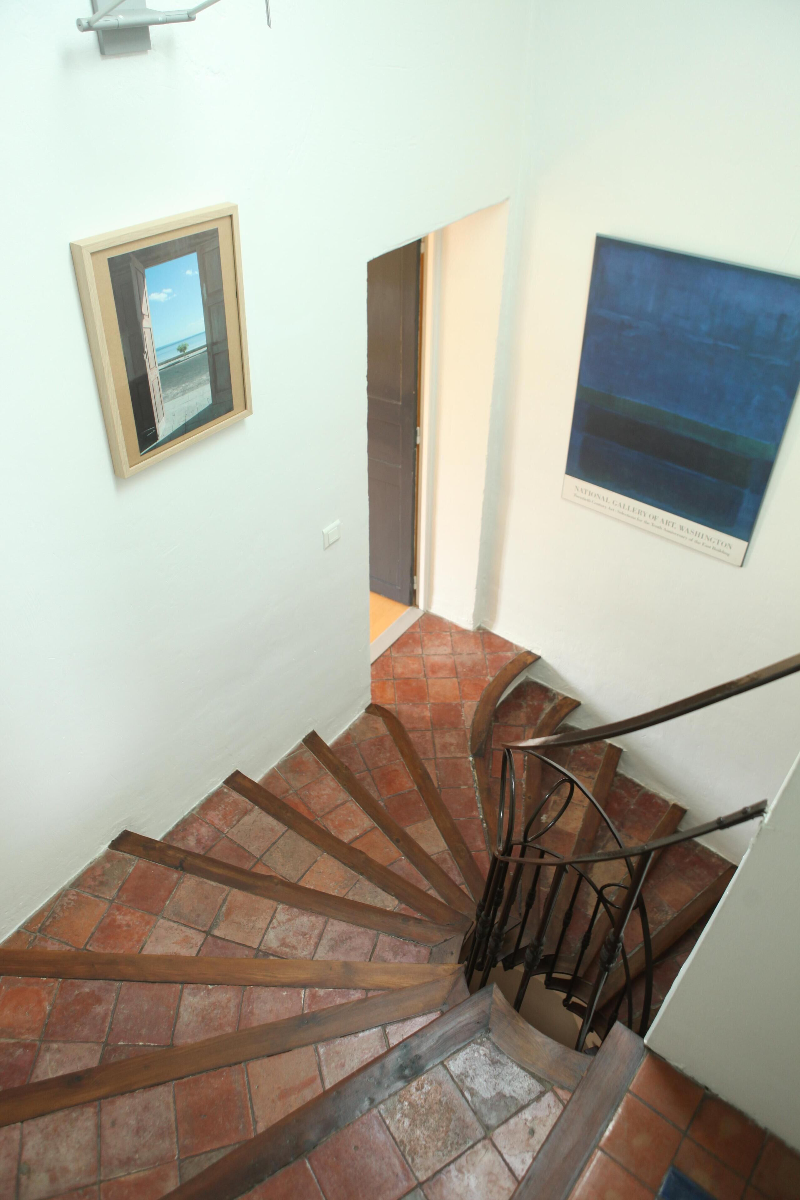 A spiral staircase with a metal handrail, a wooden frame picture on the wall, and a tiled floor.