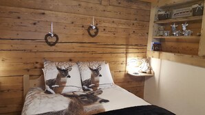 Une chambre de style cabane en bois, avec un lit agrémenté d’une literie sur le thème des cerfs, une étagère avec des objets décoratifs et deux couronnes accrochées au mur.