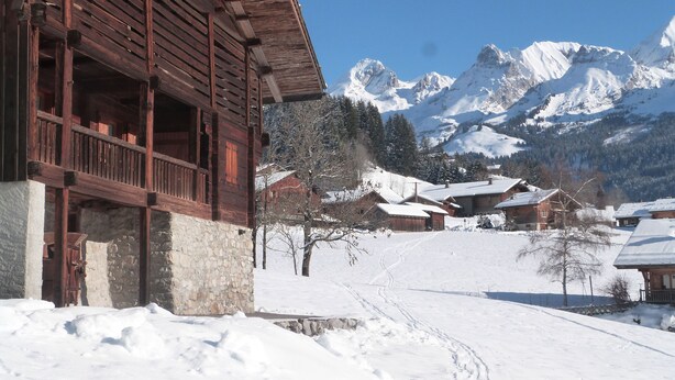 Un bâtiment en bois doté d’un balcon, entouré d’un paysage enneigé et avec des montagnes en arrière-plan.
