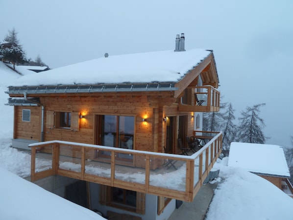 A wooden chalet with a balcony, large windows, and a chimney.