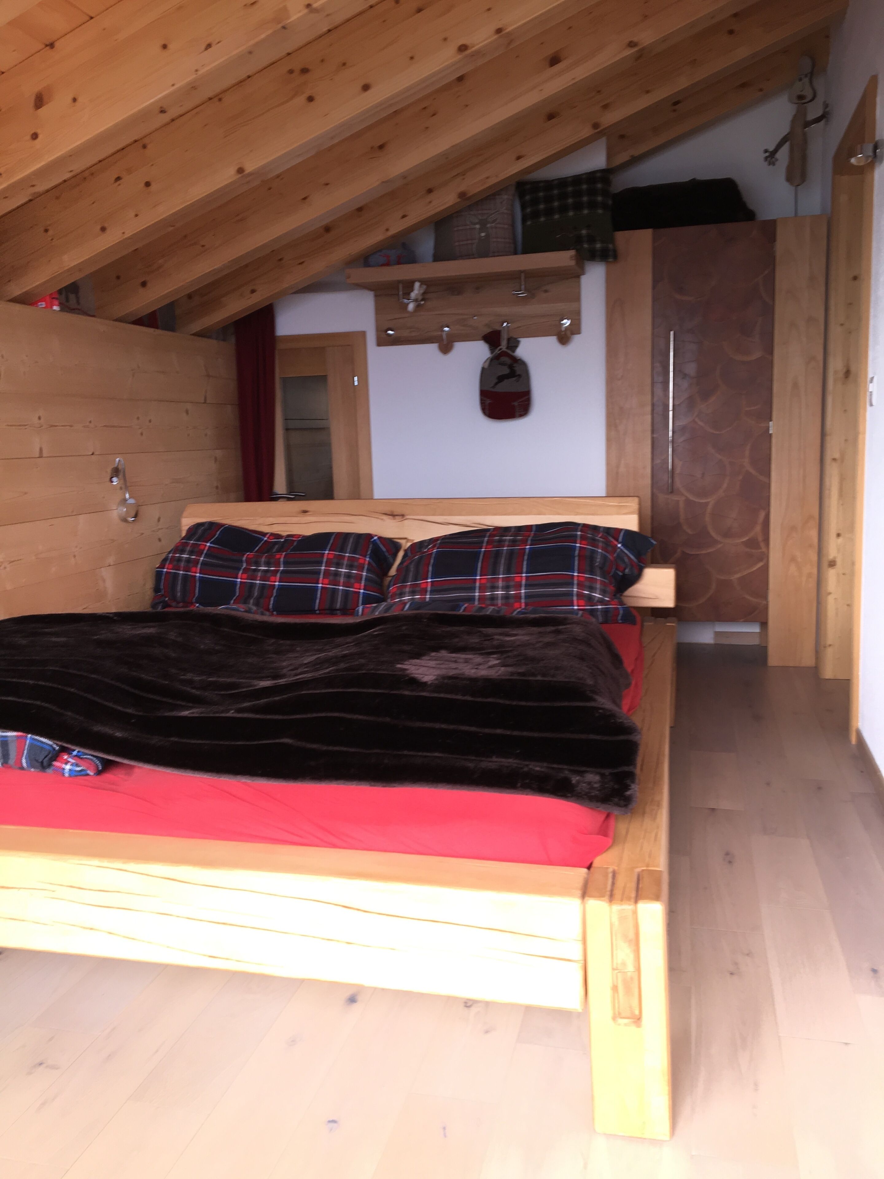 Ein hölzernes Bett mit roter Decke und Karottenkissen in einem Zimmer mit Holzwänden und geneigter Decke.