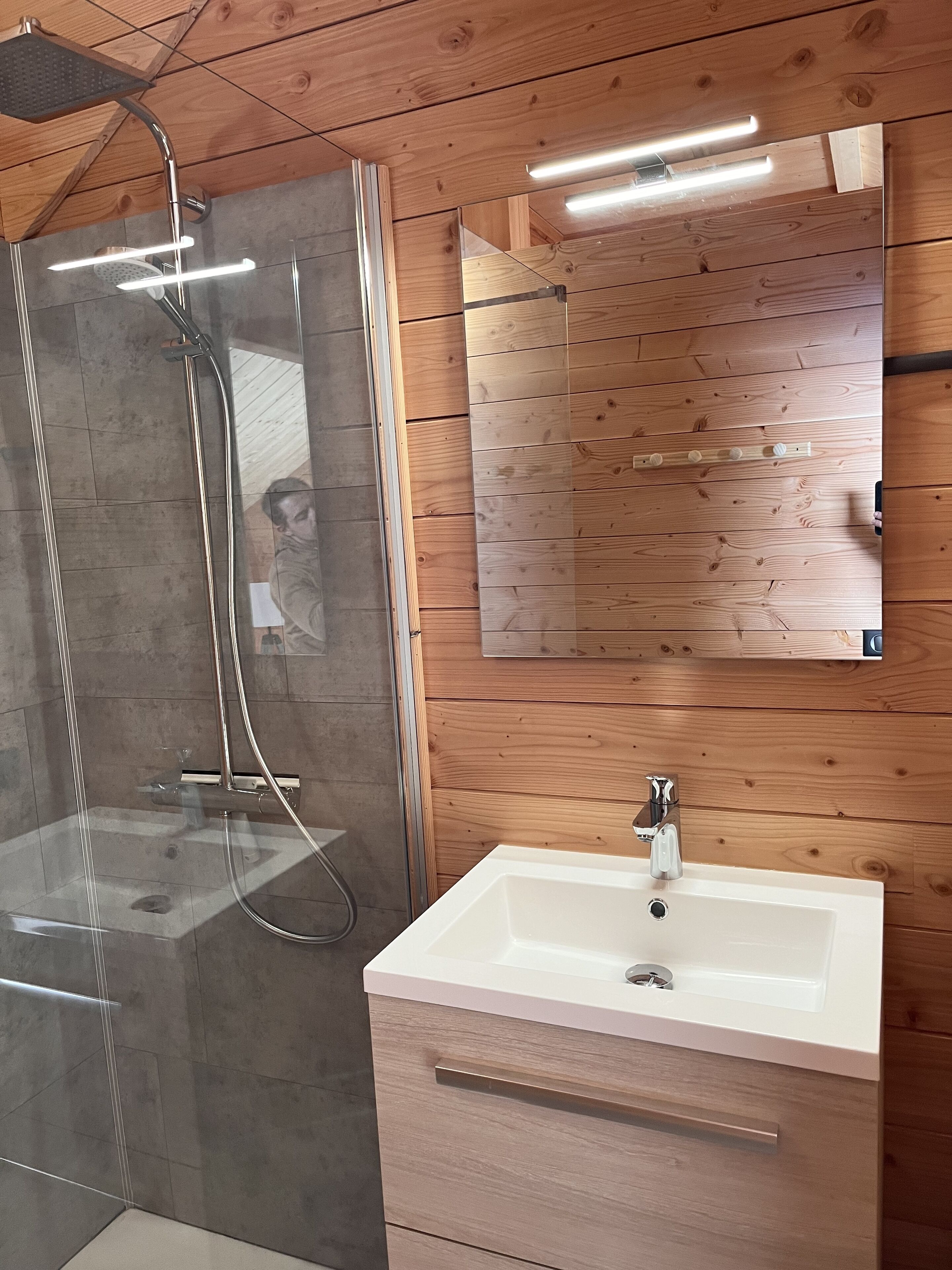 Une salle de bain moderne avec une douche à parois de verre, un lavabo blanc et un meuble-lavabo en bois.