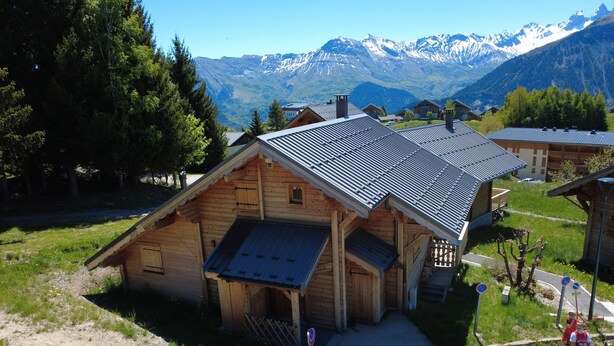 Een houten chalet met een schuin dak, omringd door een parkeerplaats en een berg op de achtergrond.