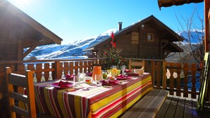 Een houten eettafel buiten, met uitzicht op besneeuwde bergen.