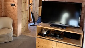 Een kamer met houten lambrisering, een televisie op een houten standaard, een stoel en een stofzuiger.