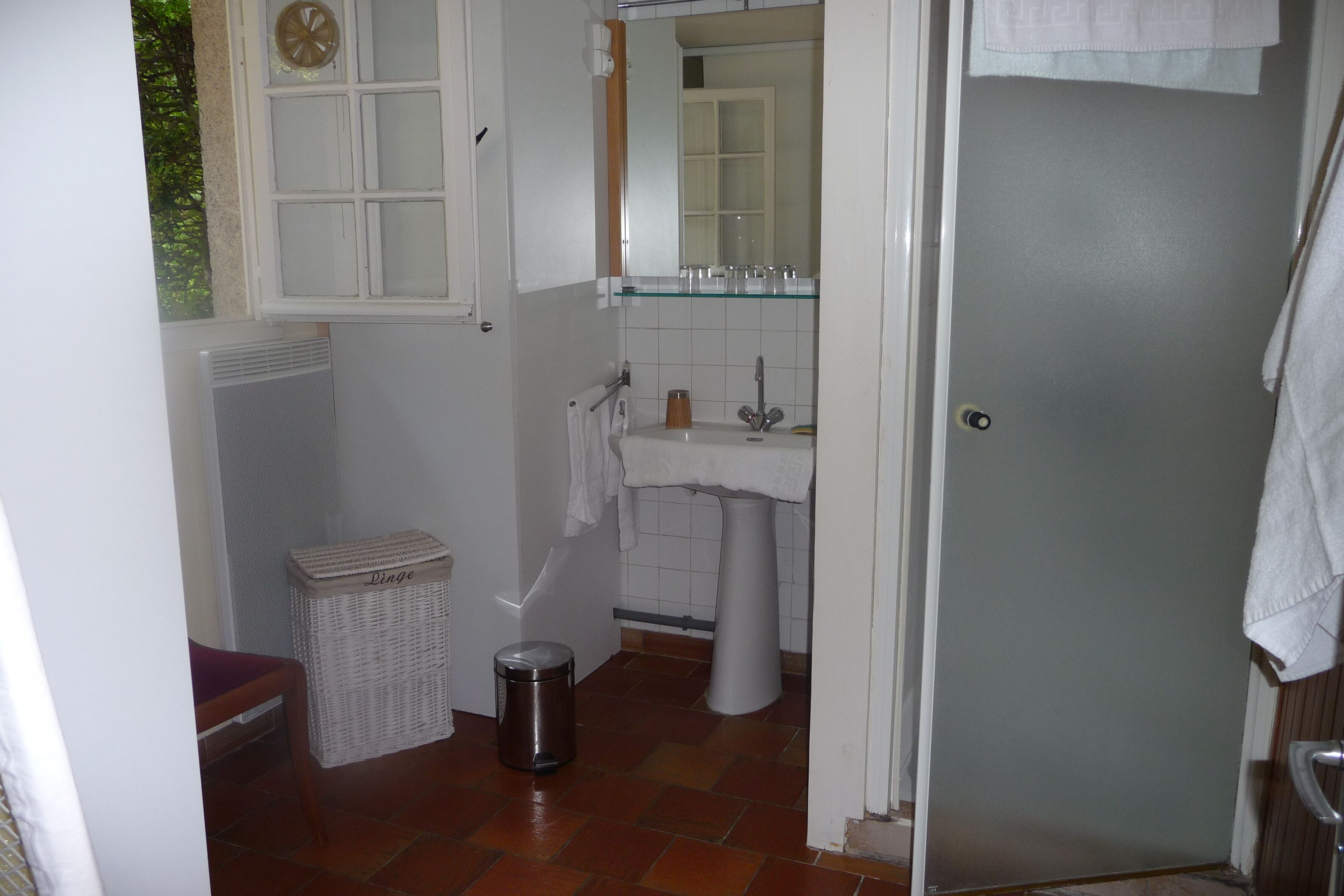 Un baño pequeño con un lavamanos blanco, un espejo y una ventana sobre el lavamanos.