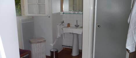Un baño pequeño con un lavamanos blanco, un espejo y una ventana sobre el lavamanos.