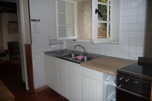 A kitchen with white cabinets, a double sink, a window with a view of a brick wall, and a built-in oven.