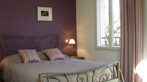A bedroom with a bed, a nightstand, a lamp, a window with curtains, and a picture on the wall.