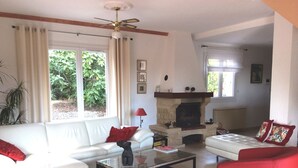 A living room with a fireplace, white sofas, red chairs, and a ceiling fan.