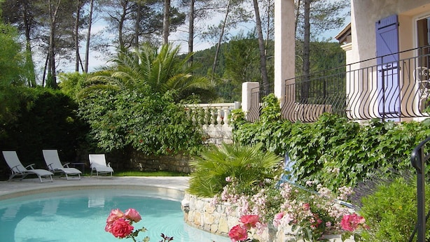 A pool area with lounge chairs, a stone wall with flowers, and a building with a balcony.