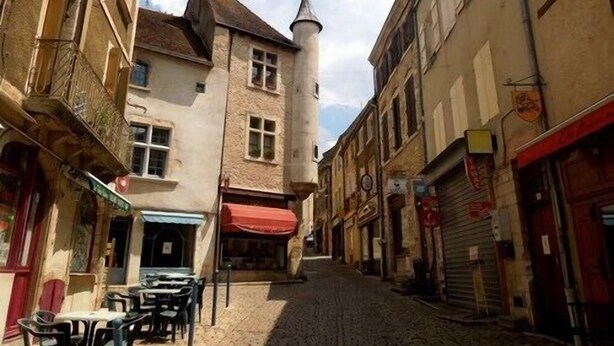 A narrow cobblestone street lined with historic buildings, some with visible shop fronts and signage.