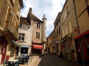 A narrow cobblestone street lined with historic buildings, some with visible shop fronts and signage.