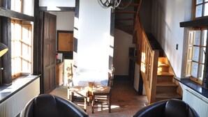 Een trap die naar een tweede verdieping leidt, houten stoelen en een tafel op de voorgrond, en een kroonluchter.