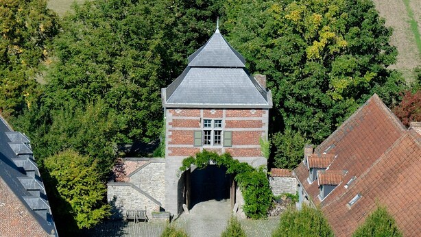Een historisch gebouw met een sterk aflopend dak, bakstenen muren en een centrale toren met een puntig dak.