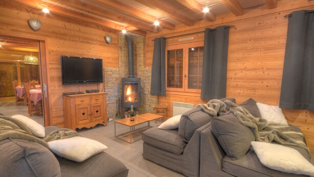 A cozy log cabin interior with a stone fireplace, wooden furniture, and a flat-screen TV.