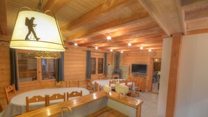 A cozy log cabin interior with a dining area, wooden furniture, and a large window.